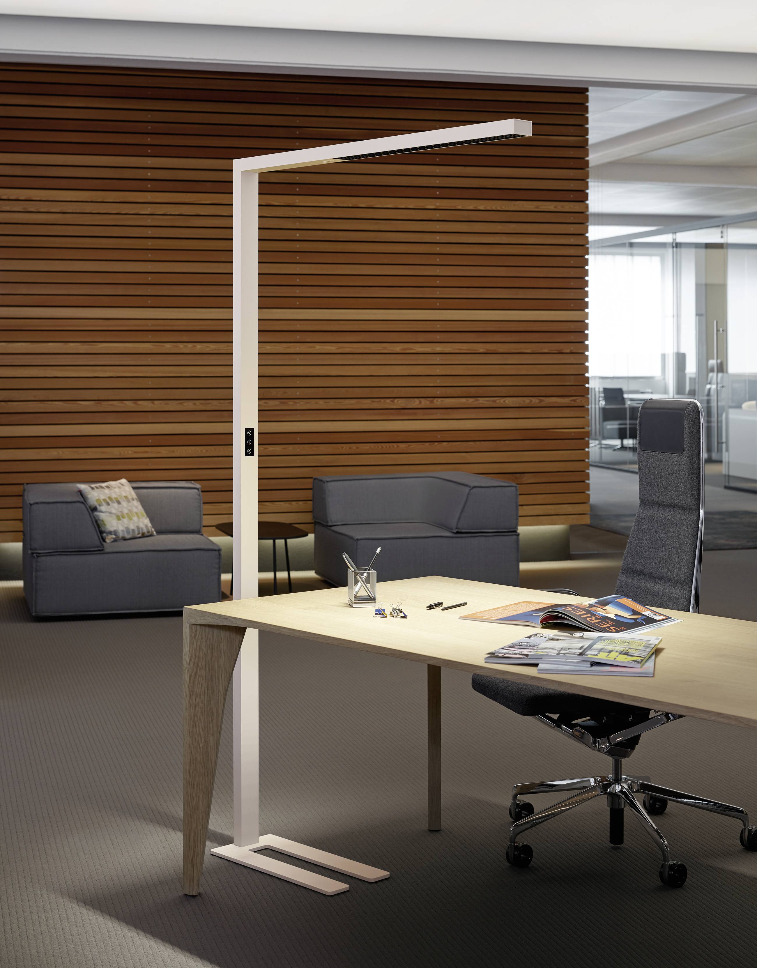 Un bureau moderne avec un bureau en bois et une lampe sur pied. Un fauteuil rembourré et un canapé sont situés à l'arrière-plan.