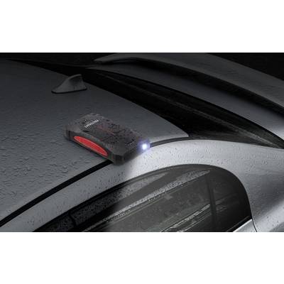 Un dispositif portable de démarrage avec lampe de poche allumée est posé sur le toit d'une voiture mouillé par la pluie.