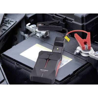 'Batterie de démarrage portable connectée à la batterie de voiture. Les pinces noires et rouges sont fixées aux bornes de la batterie.'