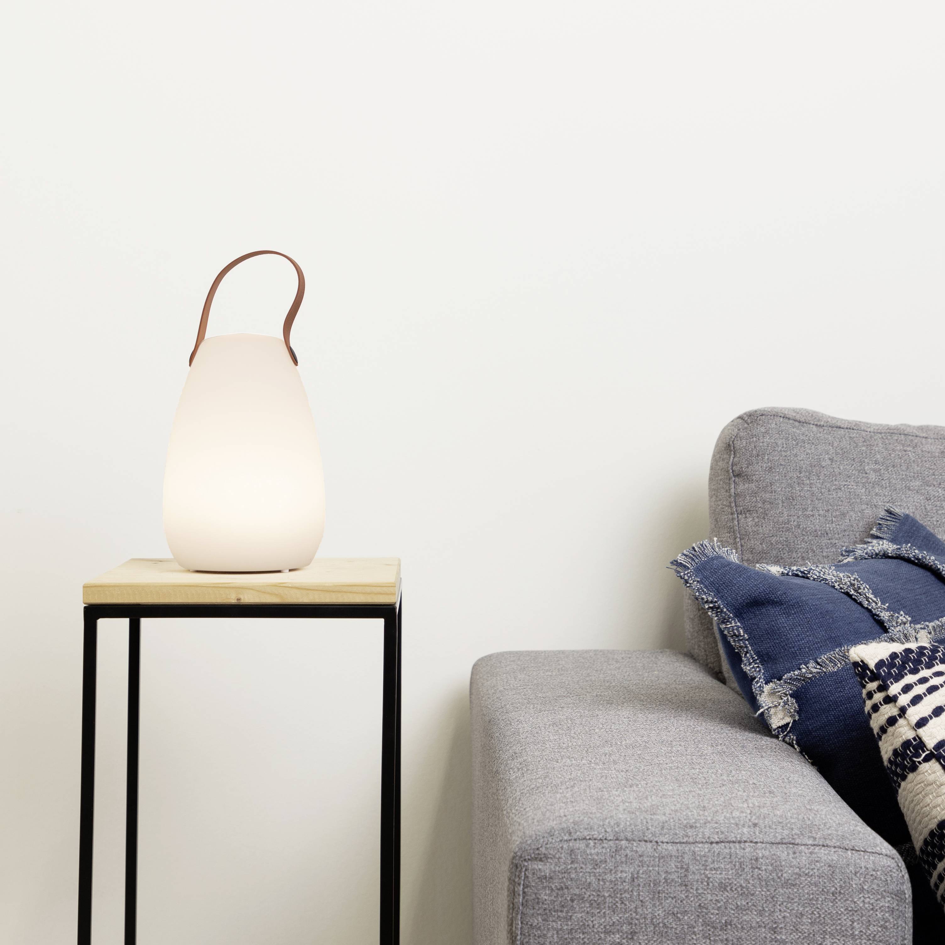 Une lampe de table illuminée est posée sur une petite table en bois à côté d'un canapé gris garni de coussins à motifs.