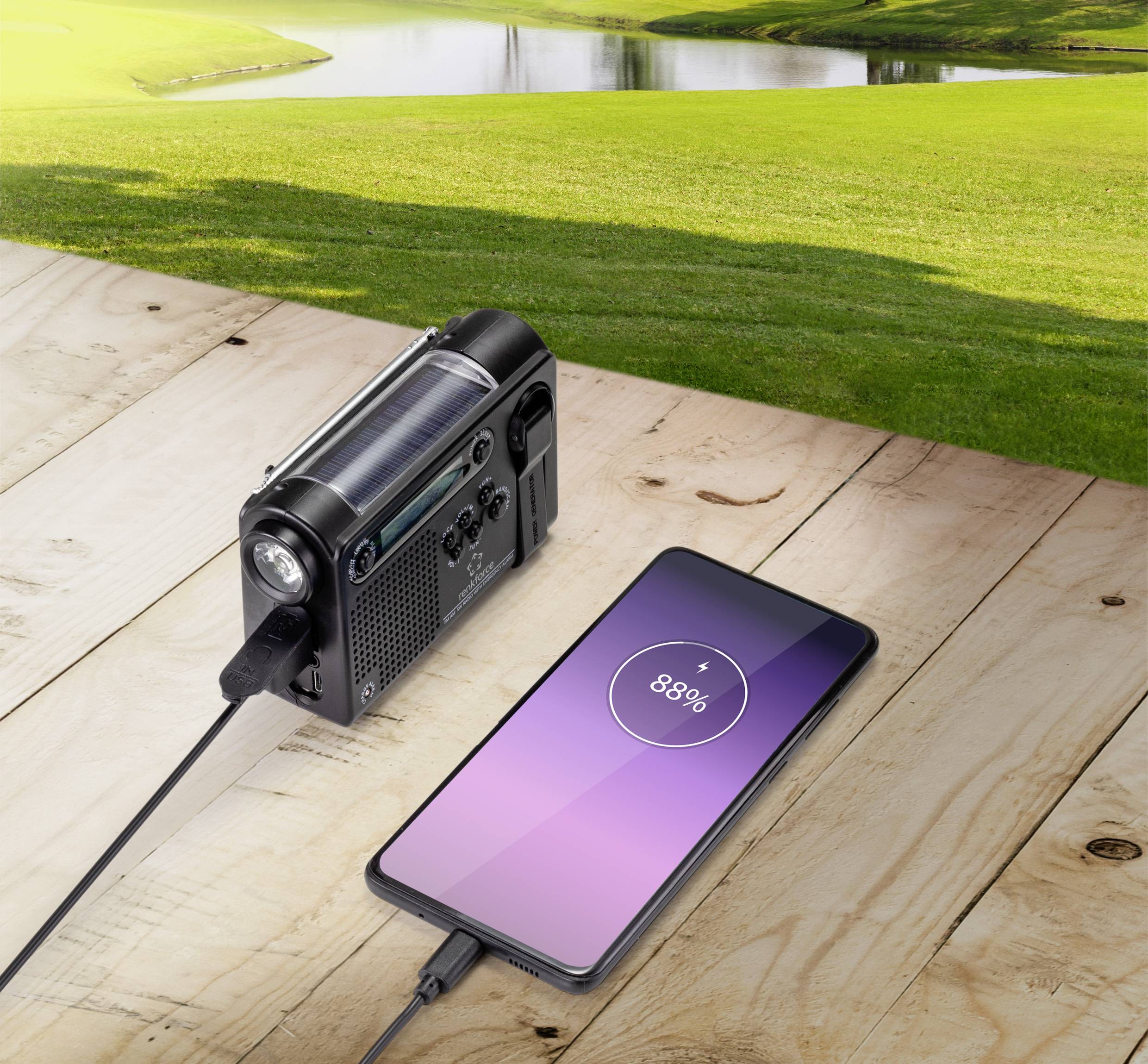 Un smartphone est en train de se charger sur une table en bois avec un chargeur solaire portable. Un paysage verdoyant est visible en arrière-plan.