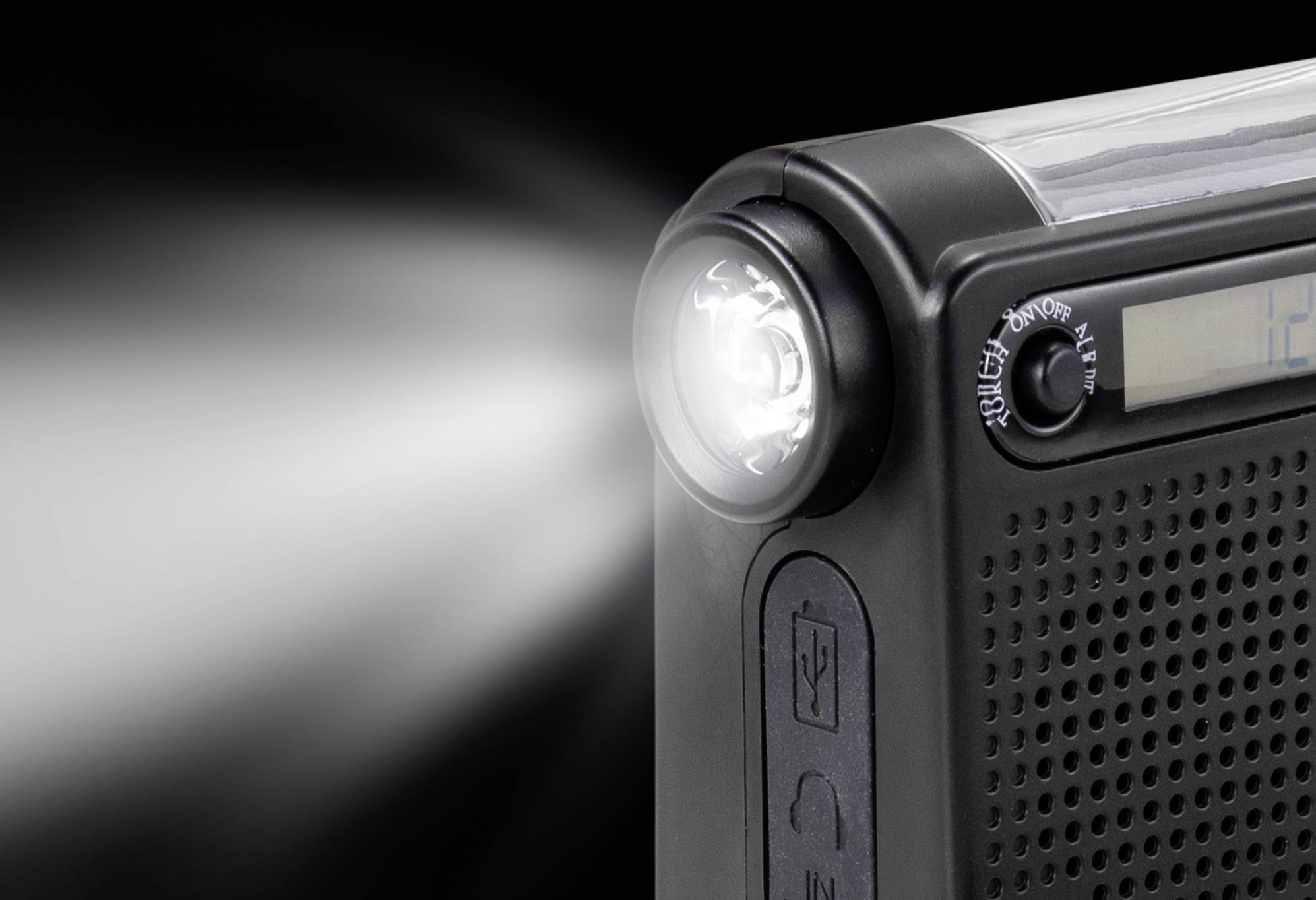 Une radio portable noire avec une lampe de poche intégrée s'illumine vivement. Un nombre est partiellement visible sur un écran.