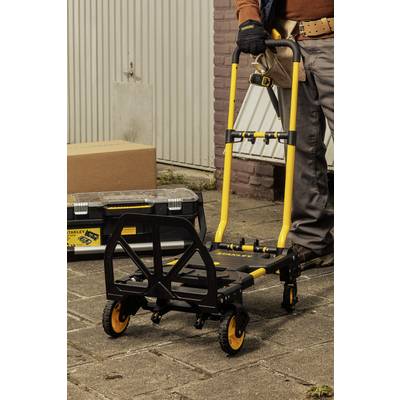 Une charrette jaune est posée sur le sol à côté d'une boîte à outils. Une personne porte des vêtements de travail et tient la charrette.