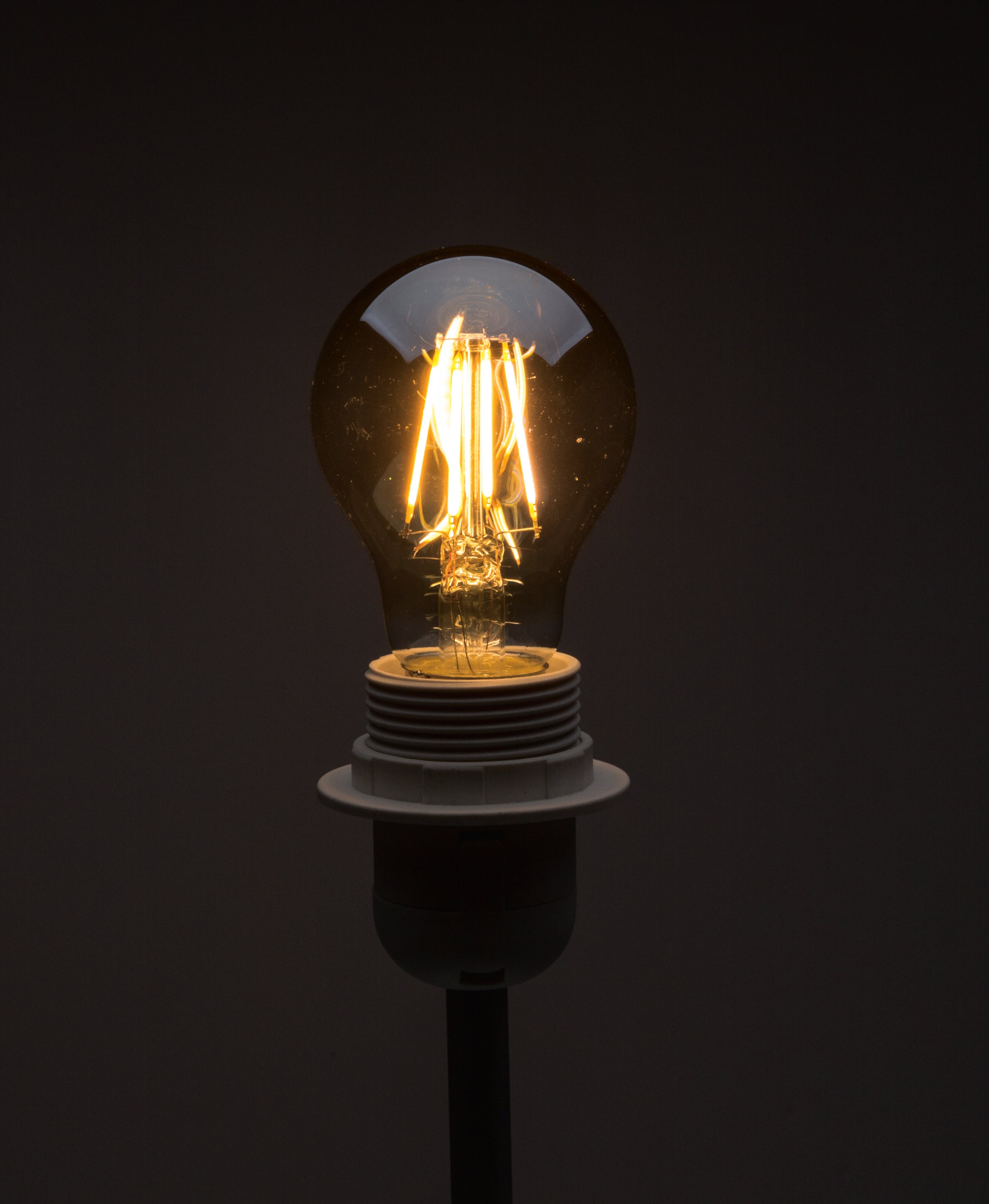 Une ampoule incandescente allumée sur un fond sombre, émettant une lumière chaude et jaunâtre.