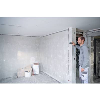 Une personne mesure le mur avec un outil laser dans une pièce en cours de finition. Travaux de construction ou de rénovation en cours.