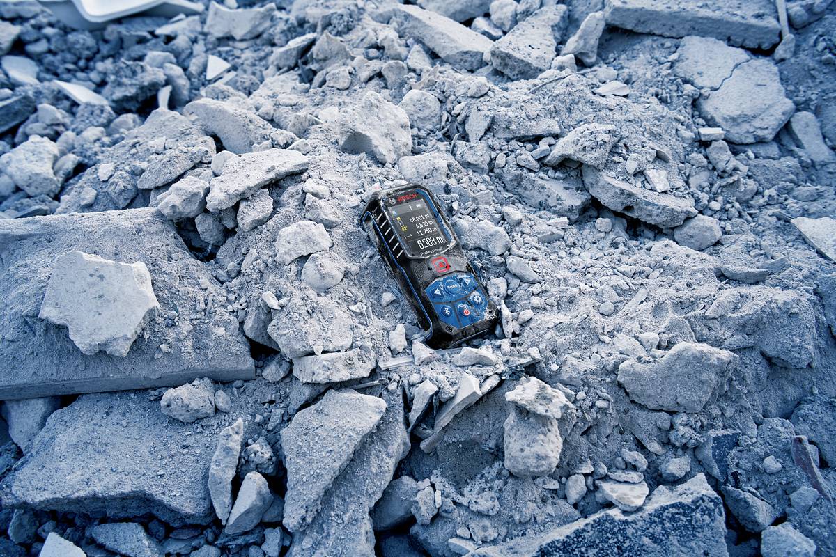 Un téléphone mobile allumé gît au milieu des décombres et des débris, entouré de blocs de béton et de poussière, dans une situation d'urgence.