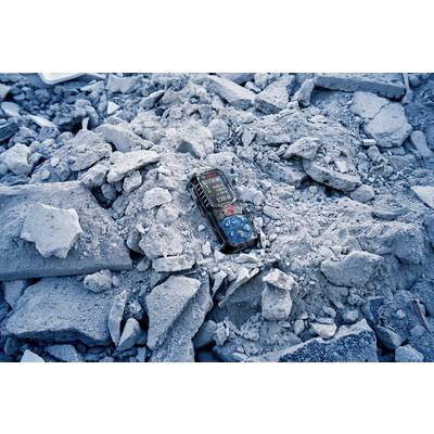Un téléphone mobile allumé gît au milieu des décombres et des débris, entouré de blocs de béton et de poussière, dans une situation d'urgence.