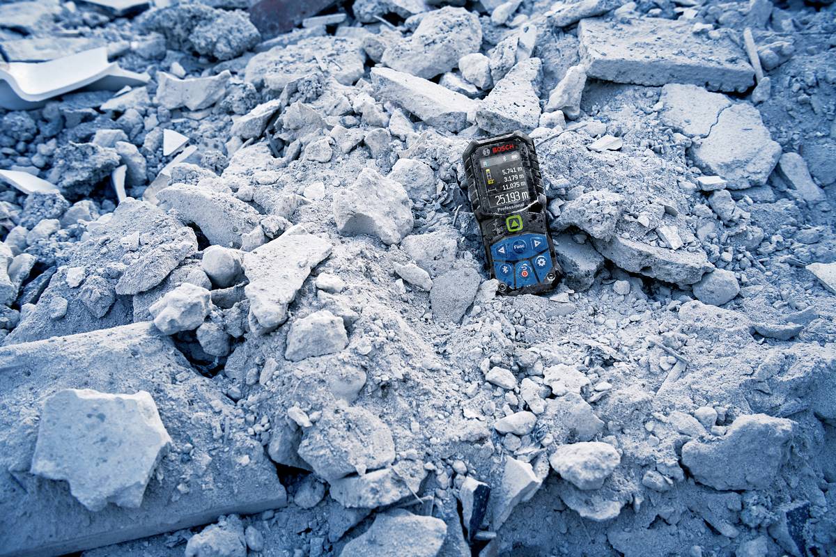 Un téléphone portable repose sur des décombres, entouré de débris et de blocs de béton, dans un environnement qui suggère une catastrophe.