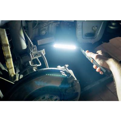 Une personne tient une lampe de poche et éclaire un essieu de voiture ou une pièce de véhicule. L'examen se fait dans un atelier.