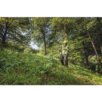 Une personne portant des vêtements de protection et un casque coupe l'herbe et les mauvaises herbes avec un débroussailleur dans une zone boisée.