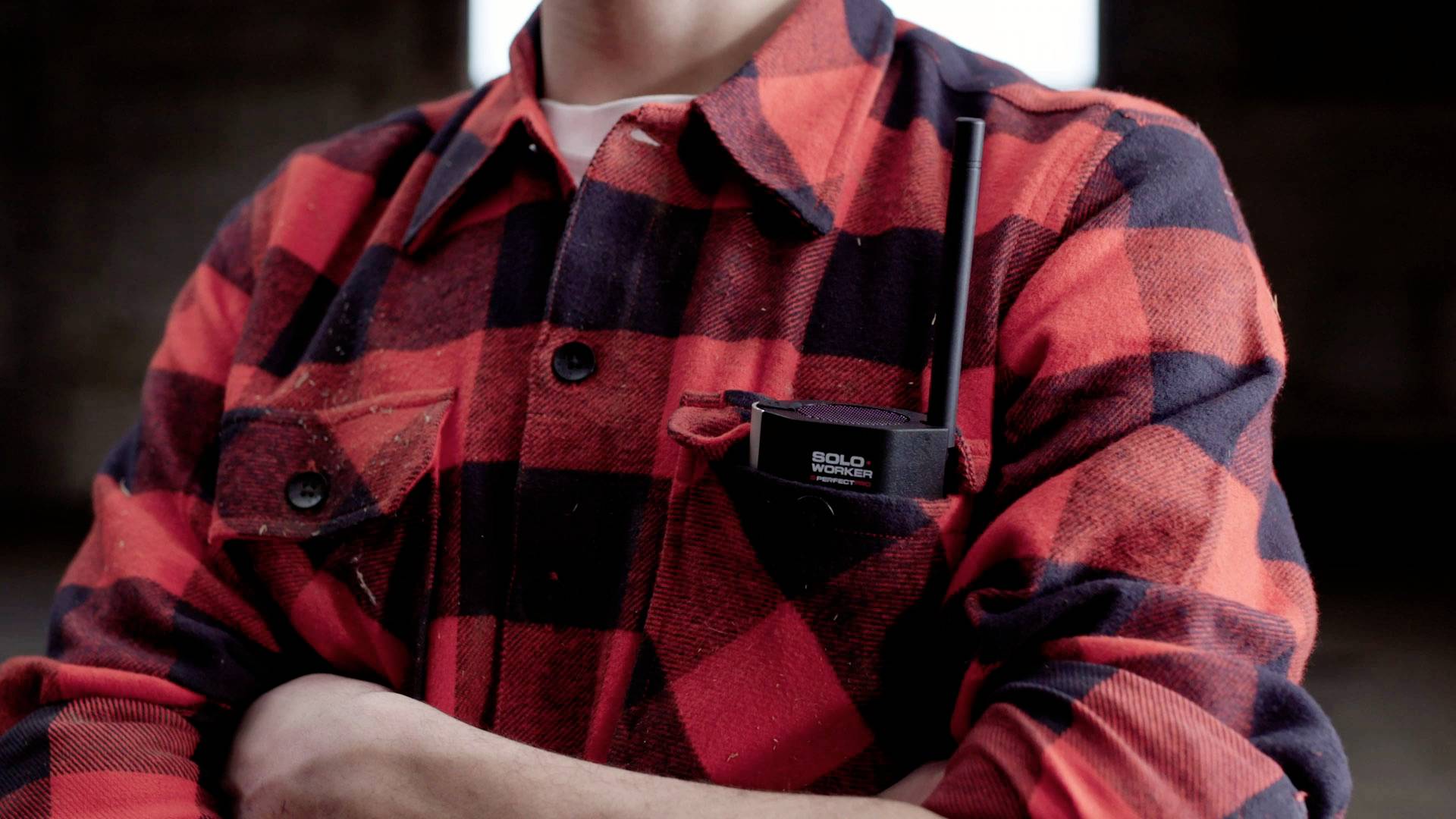 Une personne portant une chemise à carreaux rouge et noir porte une radio à la poitrine.