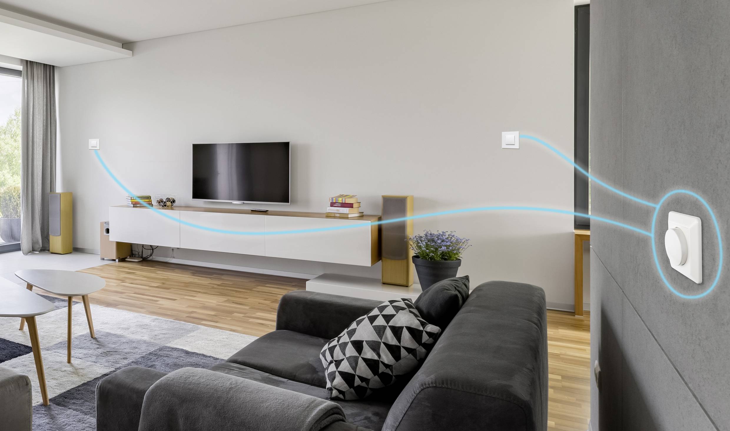 Un salon moderne avec un canapé, un téléviseur accroché au mur, et un thermostat numérique sur le mur de droite. Un câble bleu indique la connexion.