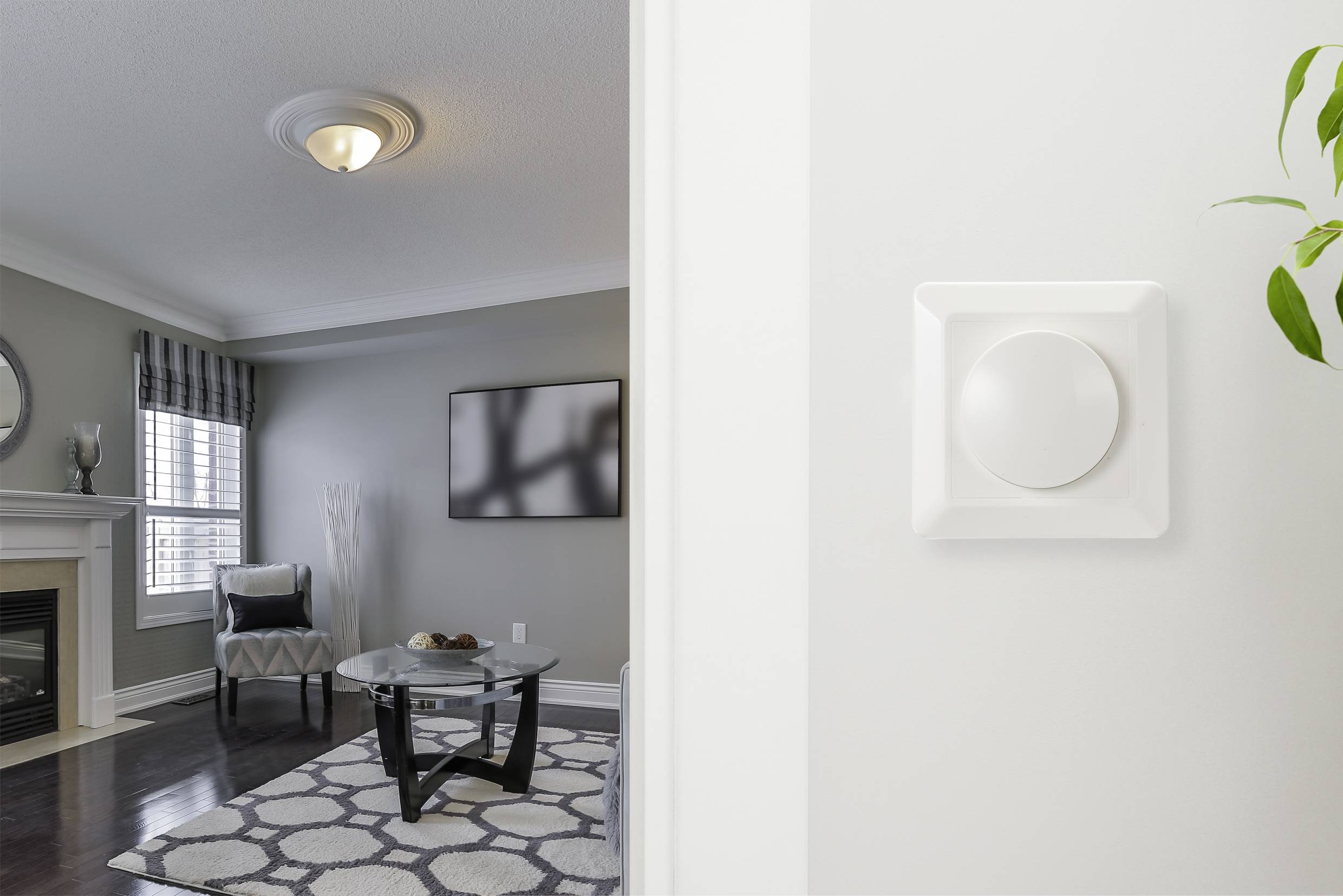 Salon avec cheminée, fauteuil et table basse moderne ; au premier plan, un thermostat rond sur le mur.