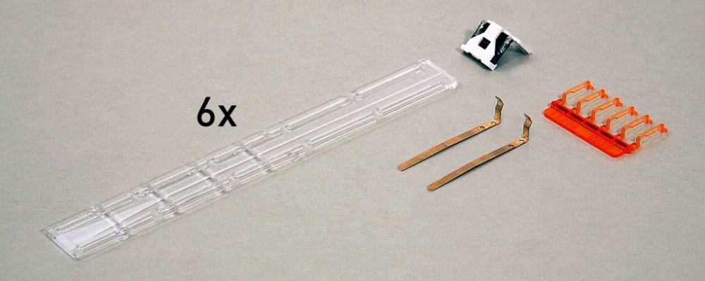 Six pièces en plastique transparentes, deux rails métalliques et un élément de connexion orange sur un fond gris.