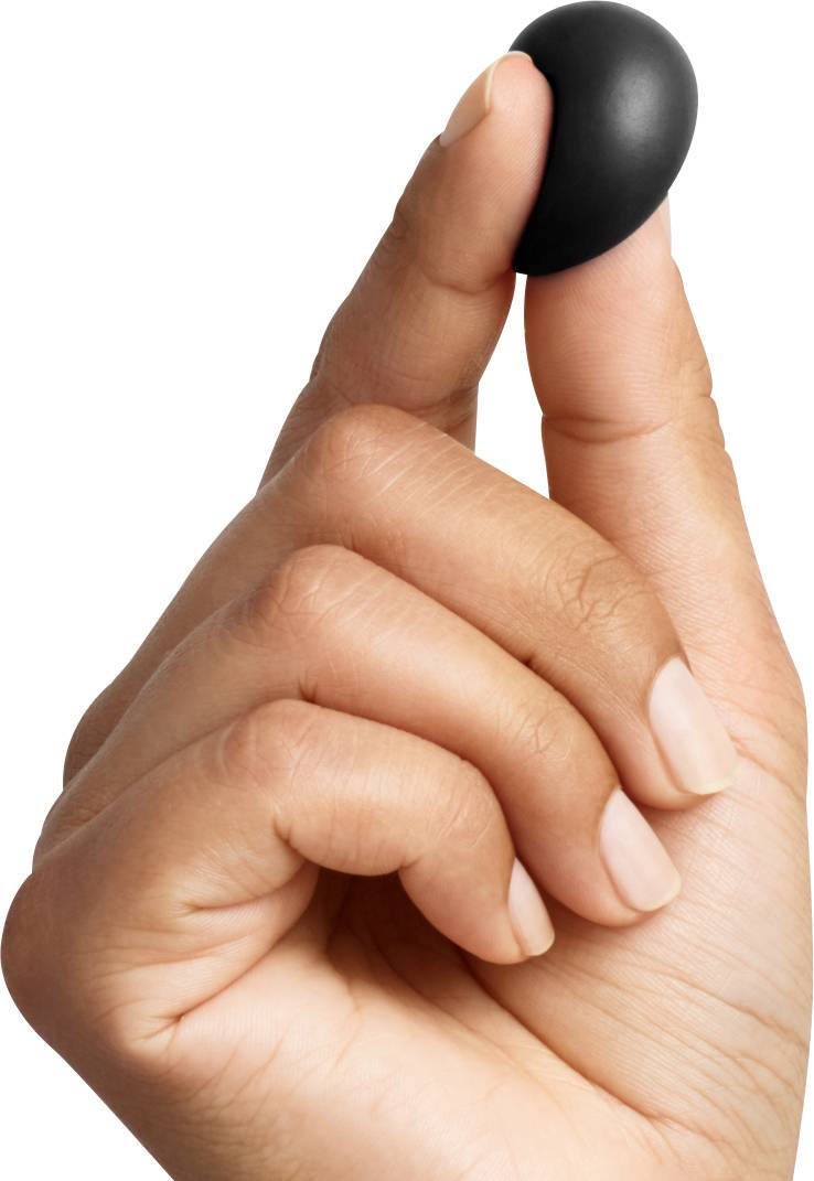 Une main tient une petite pilule noire entre le pouce et l'index.