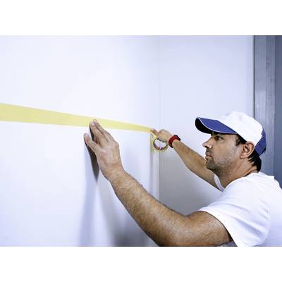 Un homme applique du ruban de masquage jaune sur un mur blanc, probablement en préparation de travaux de peinture.