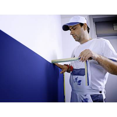 Un homme portant des vêtements de travail de peintre mesure le mur bleu fraîchement peint avec un rapporteur d'angle.
