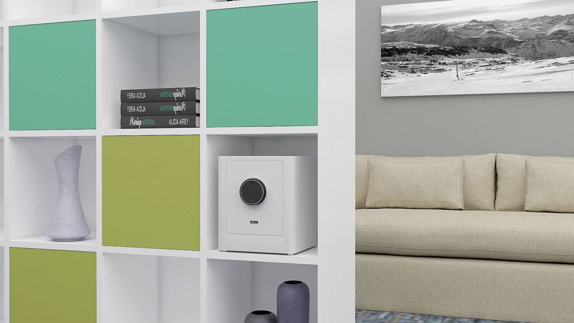 Un salon moderne avec une étagère blanche. Dans les compartiments de l'étagère, on peut voir des tiroirs colorés, des livres et un coffre-fort. À l'arrière-plan se trouve un canapé beige. Une photo en noir et blanc est accrochée au mur.