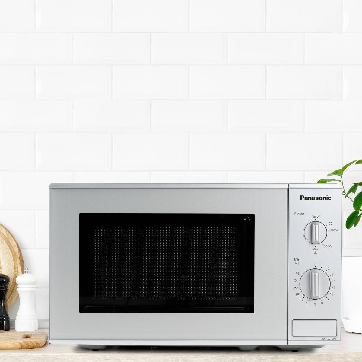 Four micro-ondes sur un plan de travail de cuisine, entouré d'ustensiles. Coquetier et planche à découper à gauche, plante à droite. Design de cuisine épuré.