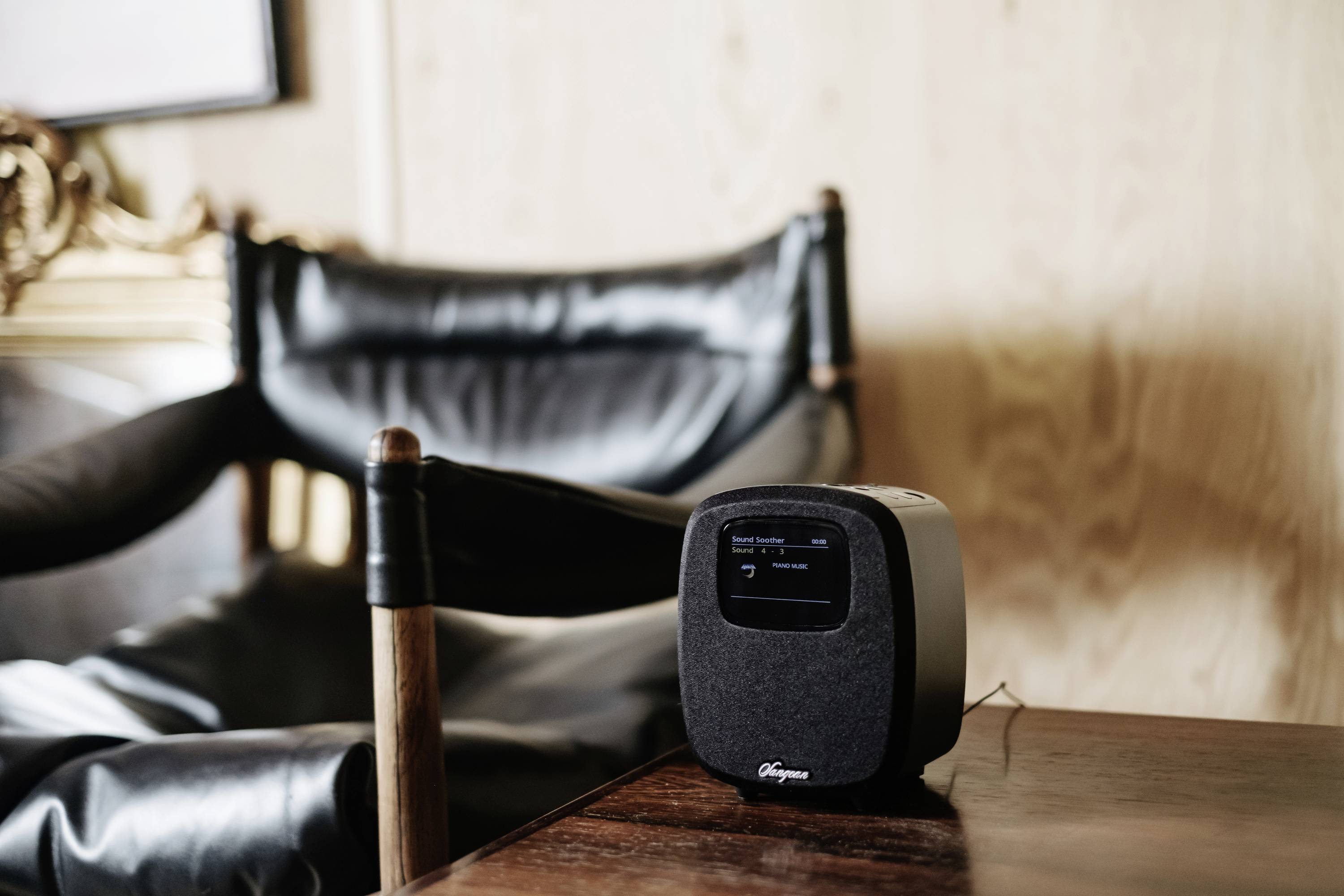 Un petit haut-parleur carré est posé sur une table à côté d'un fauteuil en cuir noir dans une pièce moderne.