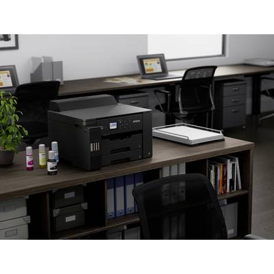 'Imprimante sur un bureau de bureau avec des chaises de bureau, des étagères et des plantes de bureau en arrière-plan, prête à être utilisée dans l'espace de travail.'