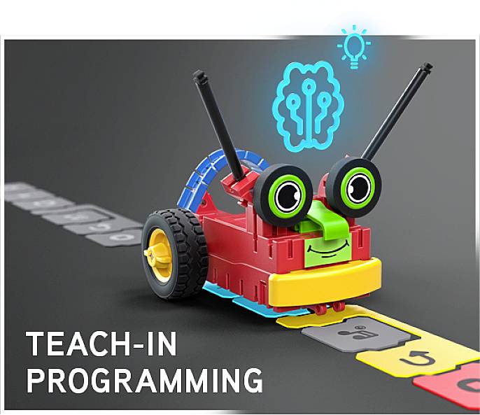 Un robot coloré composé de blocs roule sur un chemin de programmation. Au-dessus, un symbole avec un cerveau et une ampoule. Texte : 'Teach-In Programming'.
