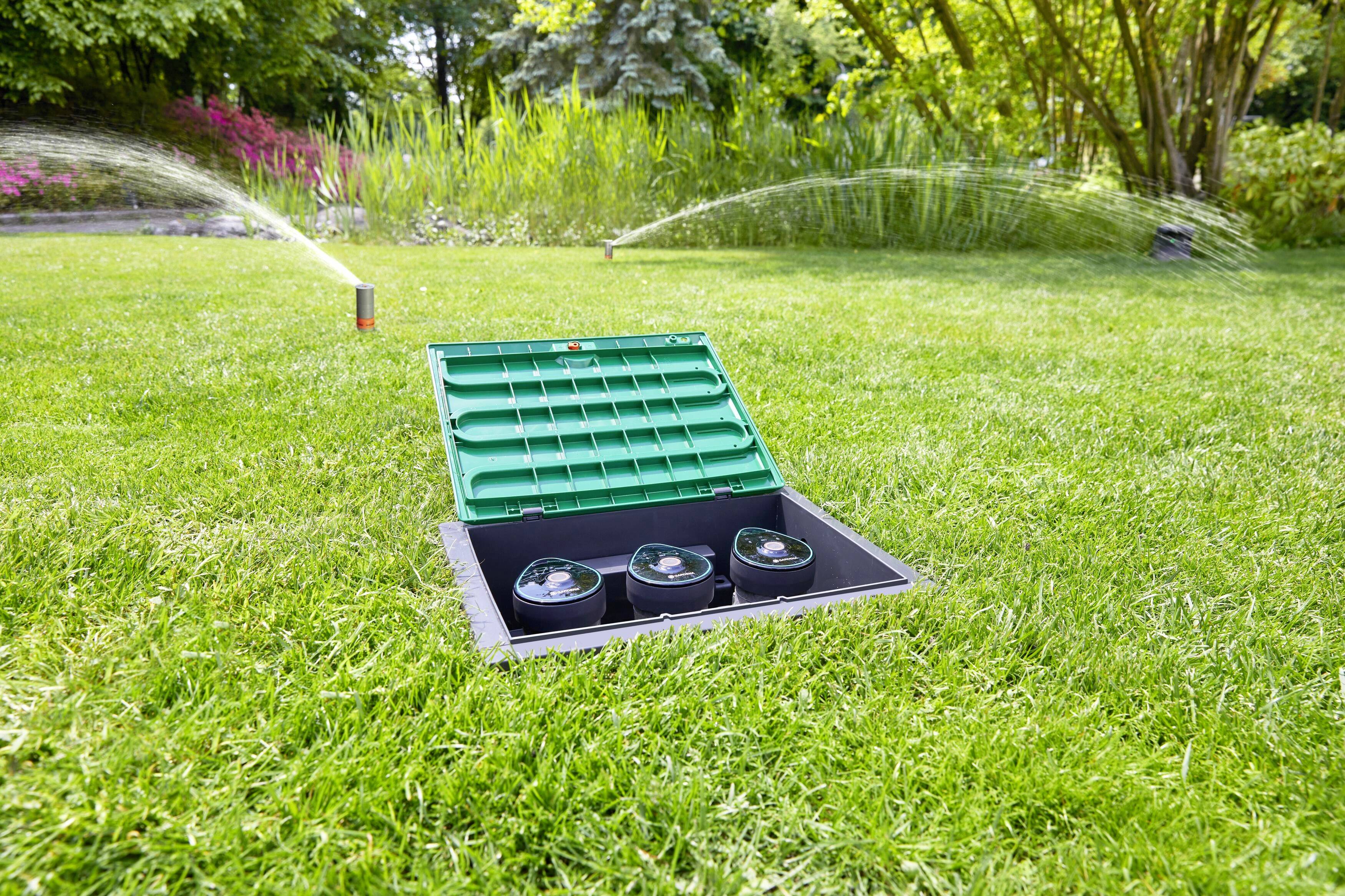 Un jardin verdoyant avec un réservoir d'eau ouvert au centre ; deux arroseurs arrosent la pelouse en arrière-plan.
