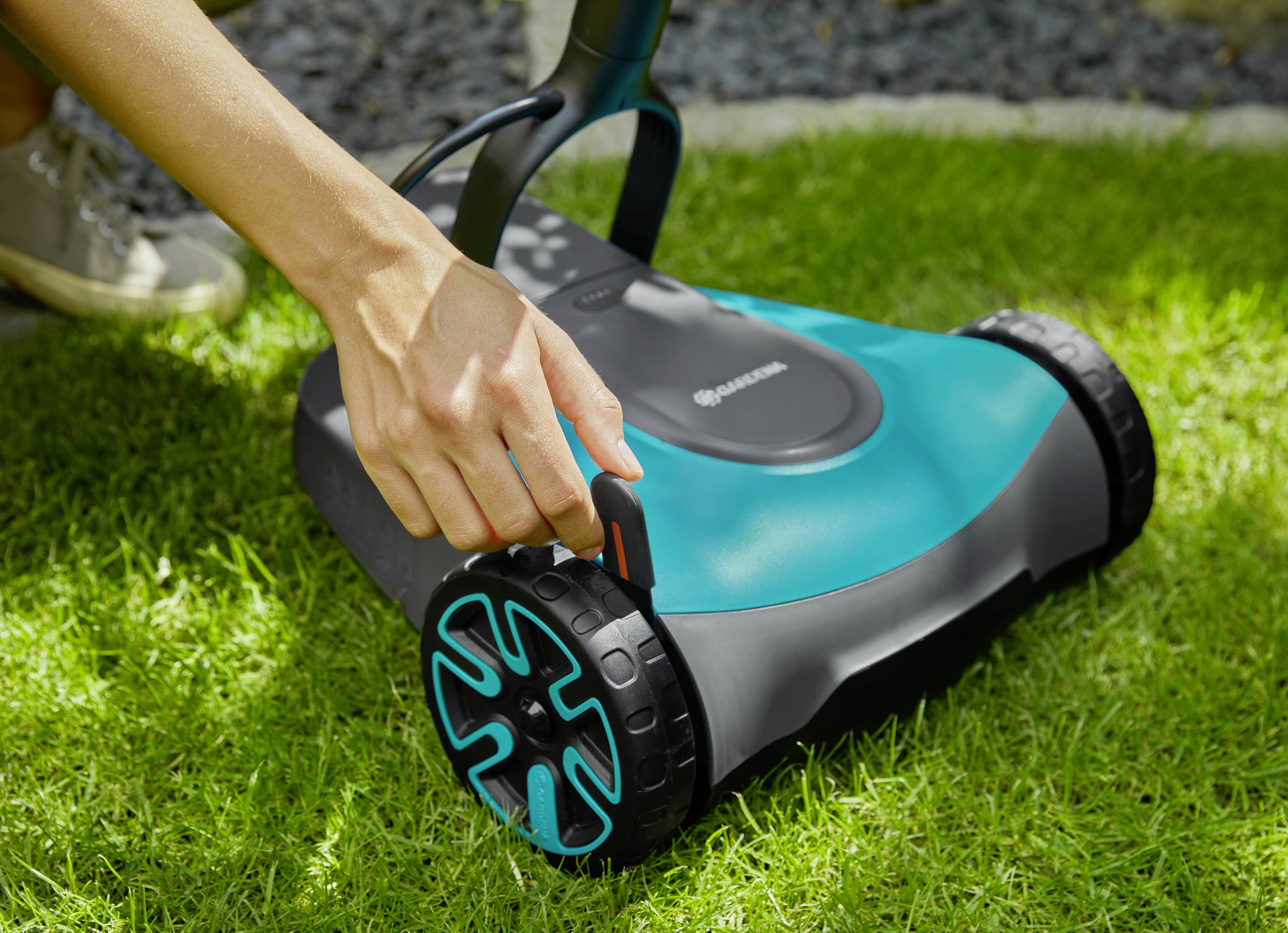 Une main règle la hauteur de coupe d'une tondeuse à gazon manuelle sur de l'herbe verte.