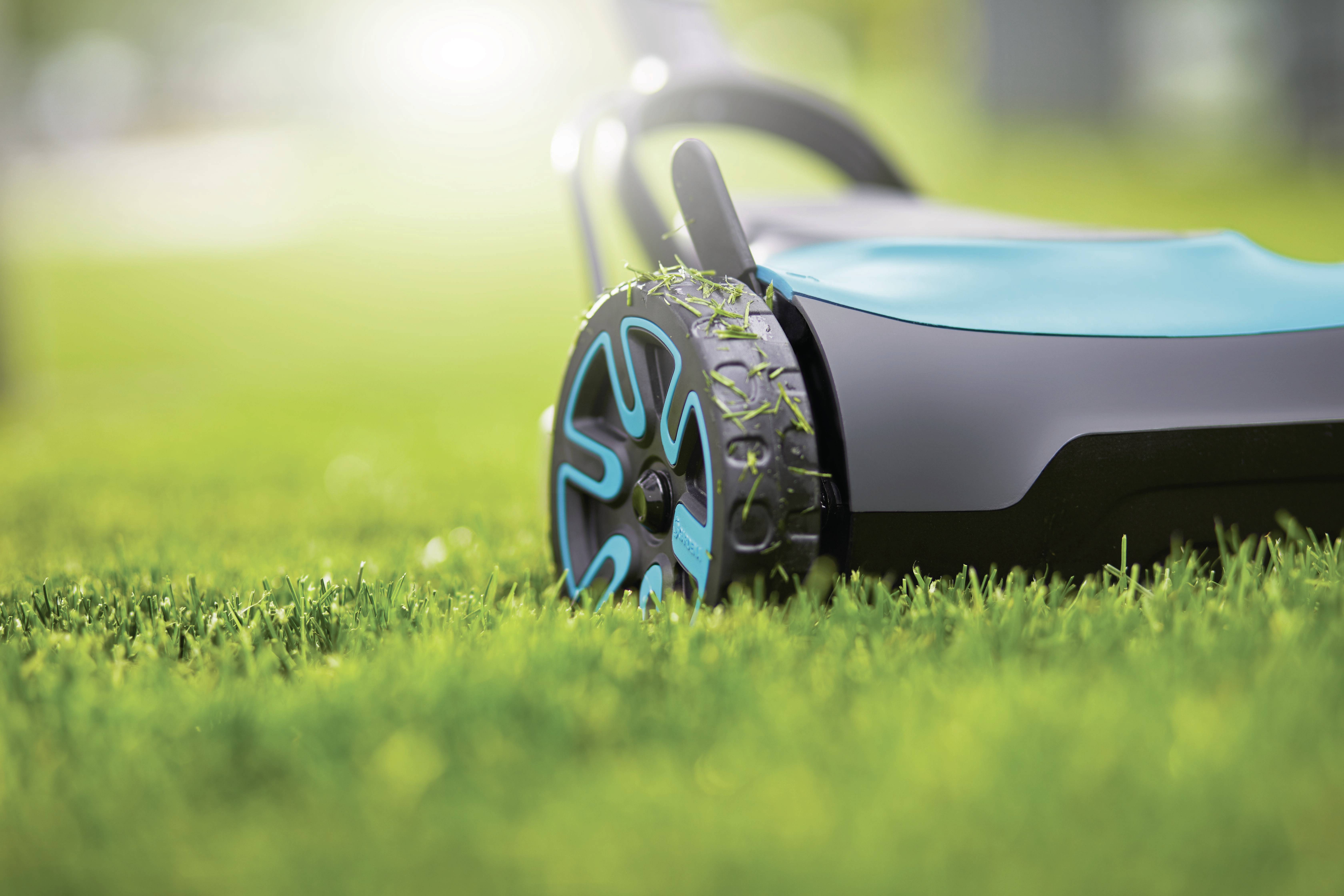 Un tondeuse moderne tond de l'herbe fraîche et verte par temps ensoleillé. L'accent est mis sur la roue, qui présente des résidus d'herbe.