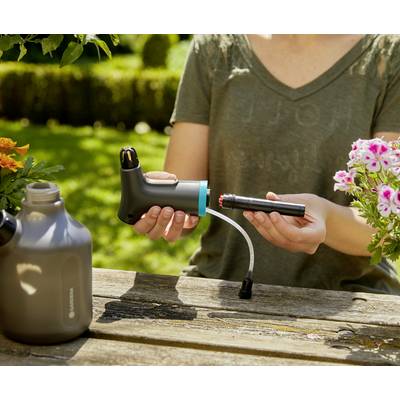 Une personne montre comment assembler un dispositif d'irrigation. Une table à l'extérieur est visible avec des fleurs et un arrosoir.