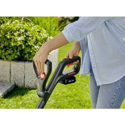 Une personne porte une chemise bleue et utilise un taille-haie électrique dans le jardin. Une pelouse verte et des plantes sont visibles en arrière-plan.