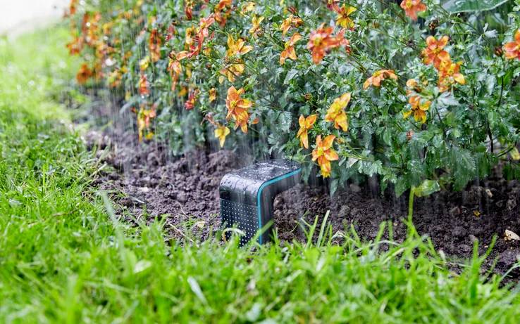 Des arroseurs automatiques arrosant un massif de fleurs avec des fleurs oranges vives et de l'herbe verte, illustrant un système d'irrigation de jardin en action.