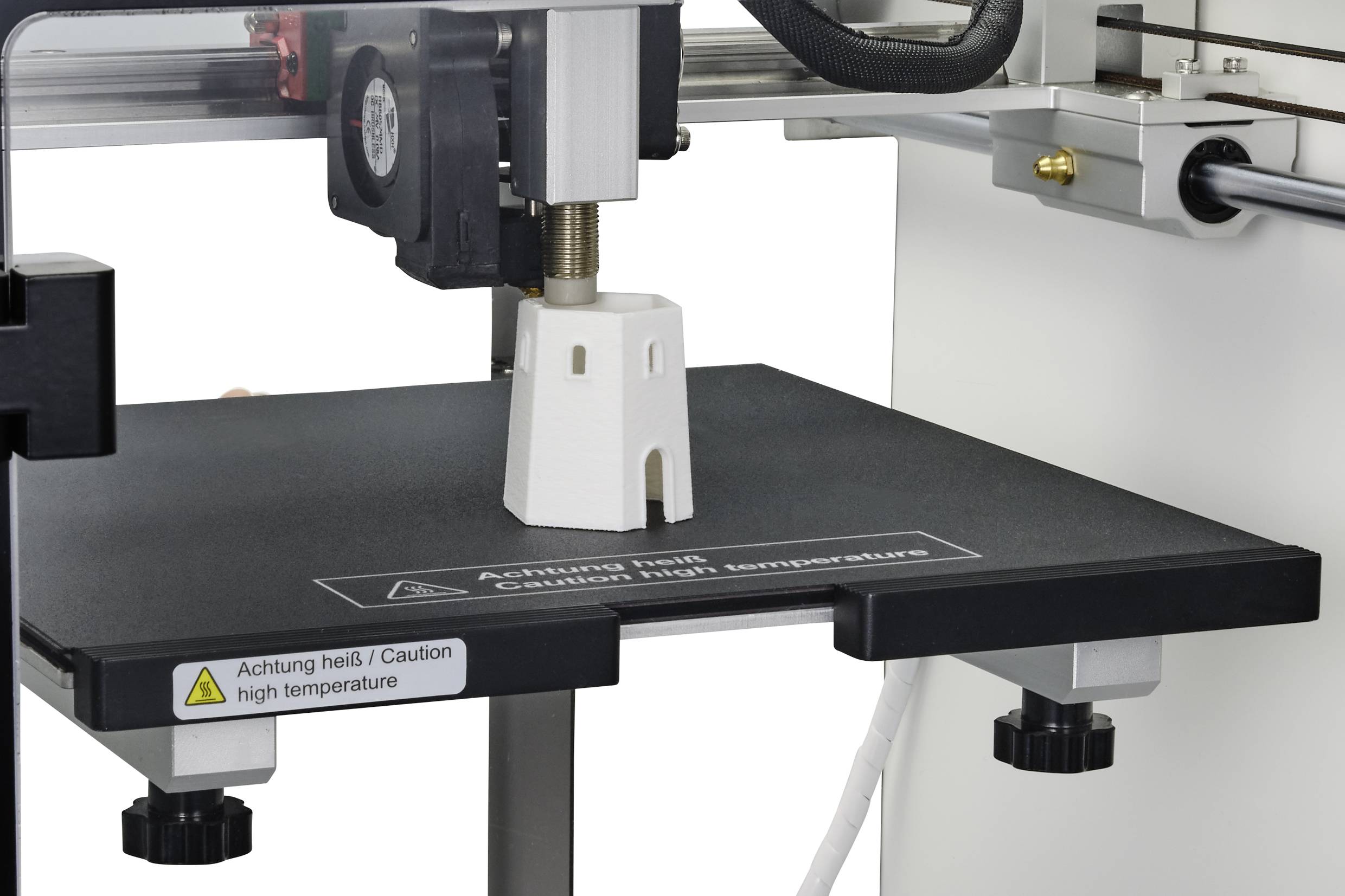 Une imprimante 3D imprime un petit objet en forme de tour en matériau blanc. Un avertissement indique une température élevée.