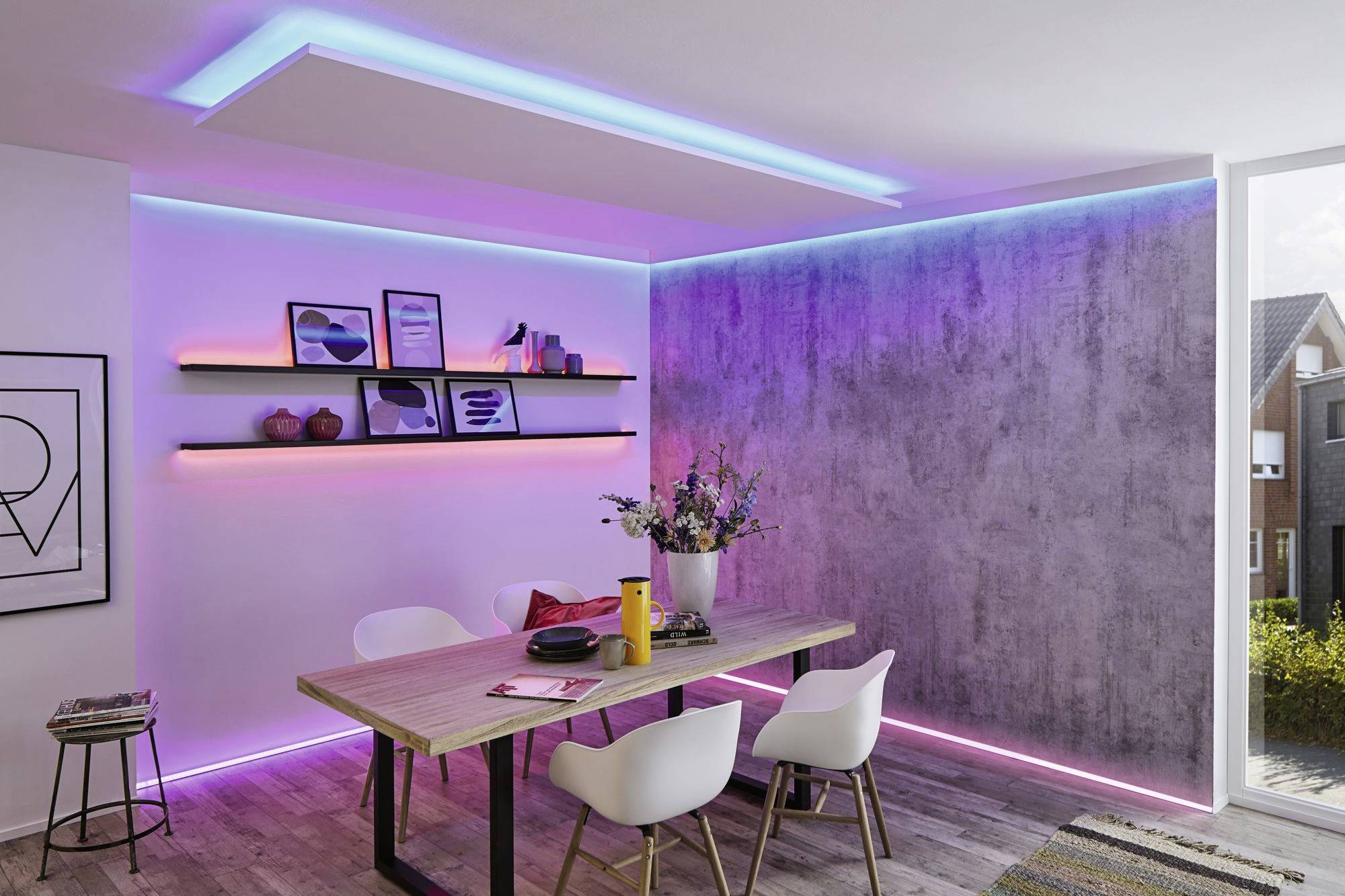 'Un espace repas moderne avec une table en bois et des chaises blanches ; des lumières LED colorées sur les murs et le plafond créent une atmosphère vibrante.'