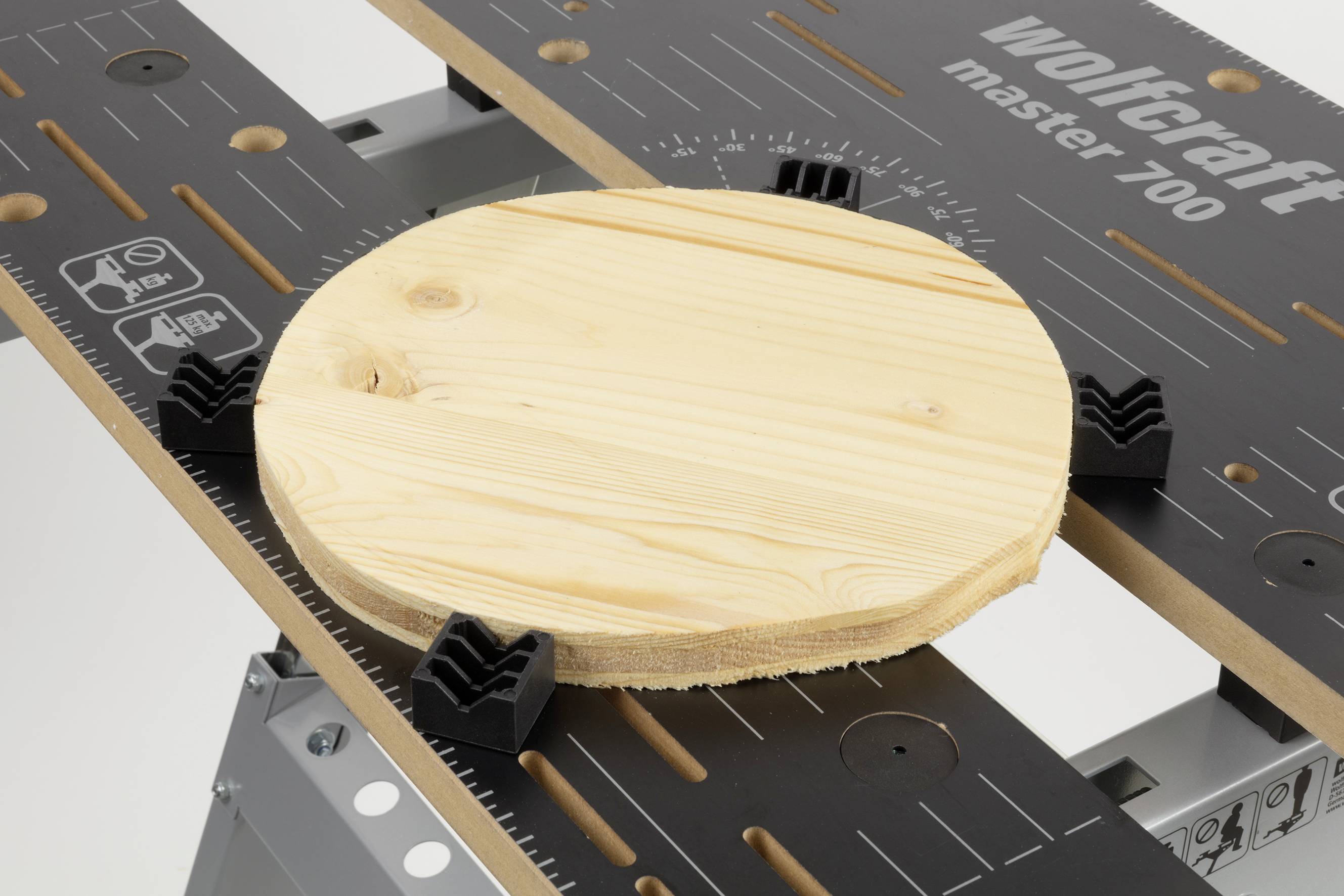 Morceau de bois rond fixé sur une table Wolfcraft Master 700, entouré de pinces pour une tenue sécurisée et un traitement précis.