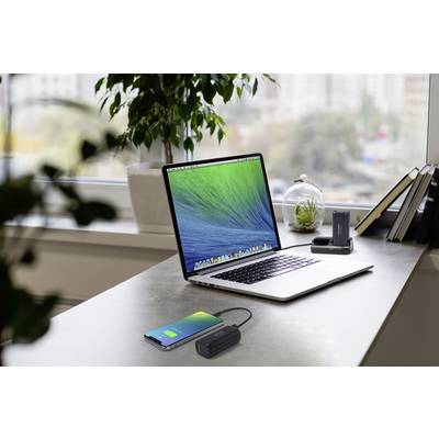 Un ordinateur portable posé sur une table dans un bureau moderne avec vue sur la ville. À côté, un smartphone et une batterie externe.