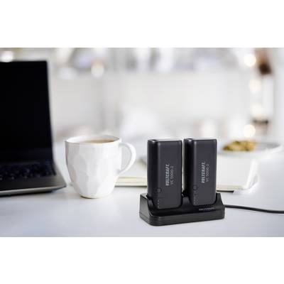 Deux batteries noires sur une station de charge à côté d'une tasse blanche et d'un ordinateur portable ouvert ; ambiance de bureau conviviale.