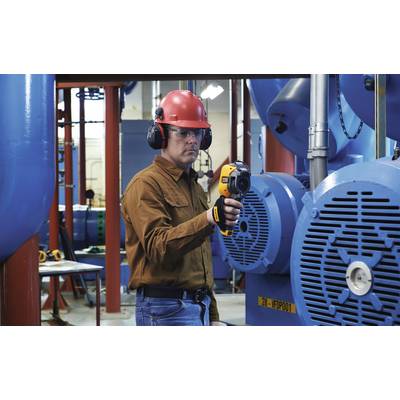 Une personne en tenue de protection vérifie les machines à l'aide d'un appareil portable dans un environnement industriel.