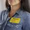Une femme porte une chemise en jean et un badge jaune sur lequel est inscrit 'Welcome', en dessous duquel on peut lire le nom 'Emily Smith, Newell Brands, Atlanta, GA'.