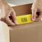 Des mains tiennent une carte jaune avec un code-barres '123456789', qui est insérée dans un carton brun.