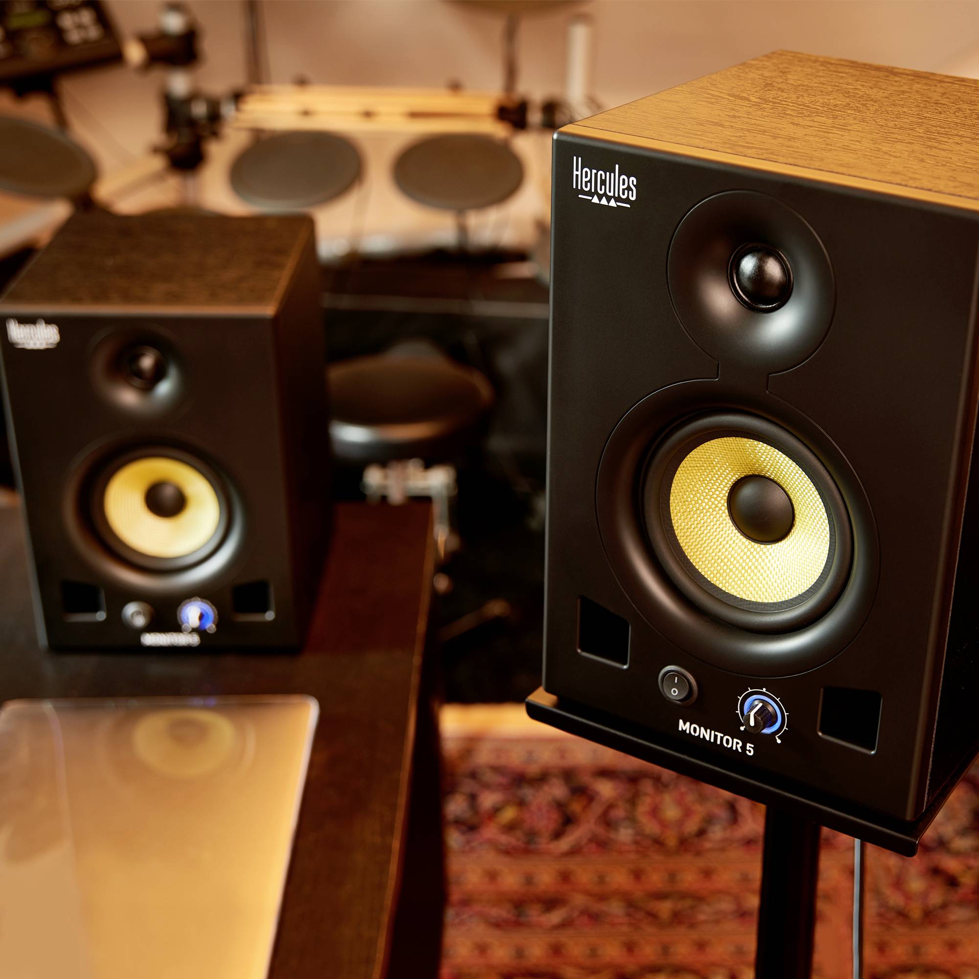 Une paire d'enceintes de 'Hercules' dans une pièce avec une batterie en arrière-plan.