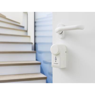 Une porte blanche avec une serrure électronique au premier plan, avec un escalier en bois et des murs bleus en arrière-plan.