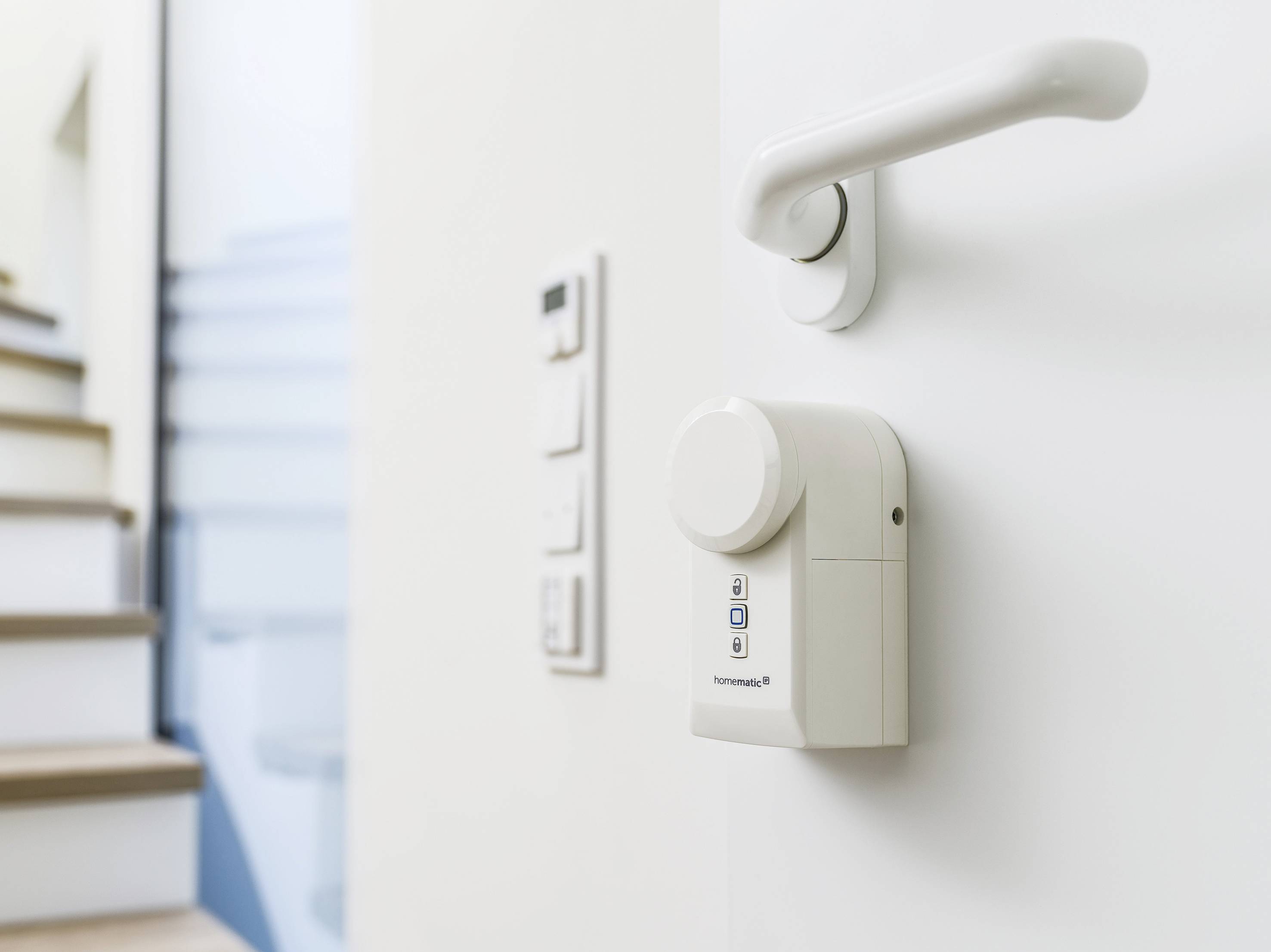 Un moteur de serrure numérique sur une porte blanche devant un escalier ; commande via des touches sur l'appareil.