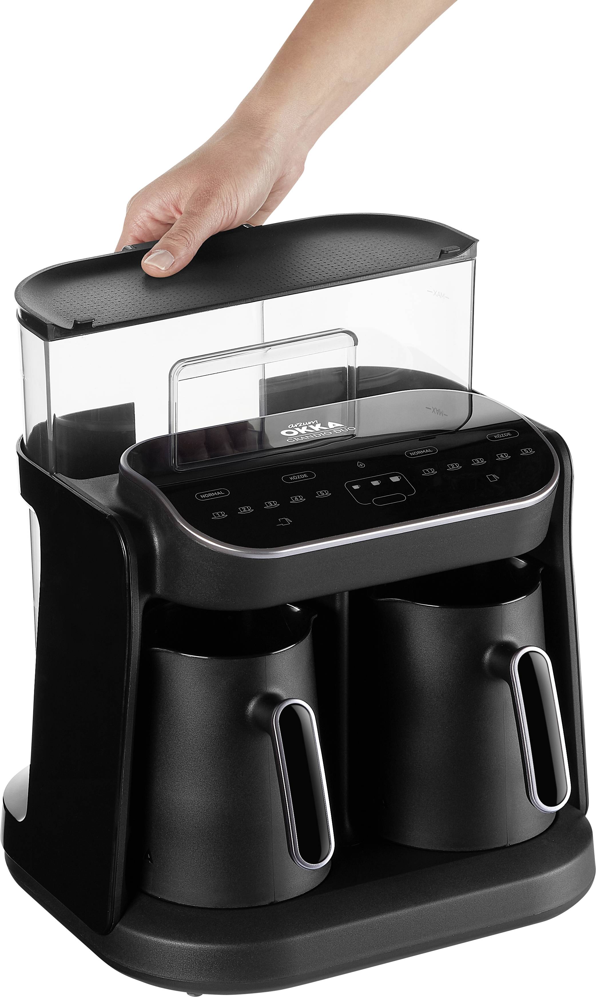 Une main soulève un couvercle d'une machine à café noire à deux carafes.