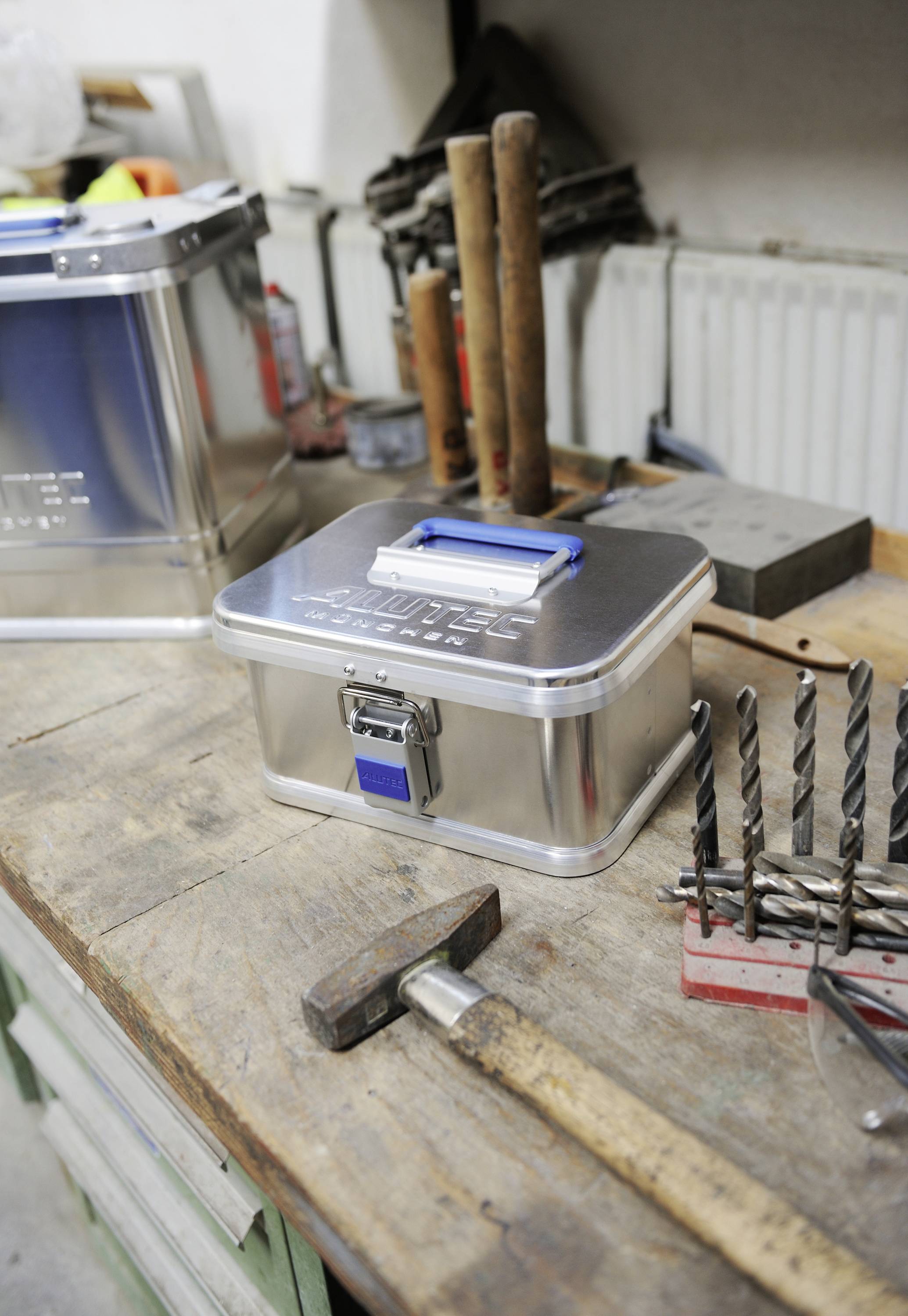 Établi avec une boîte à outils en métal, marteau et perceuse. D'autres outils sont visibles en arrière-plan. Ambiance d'un atelier.