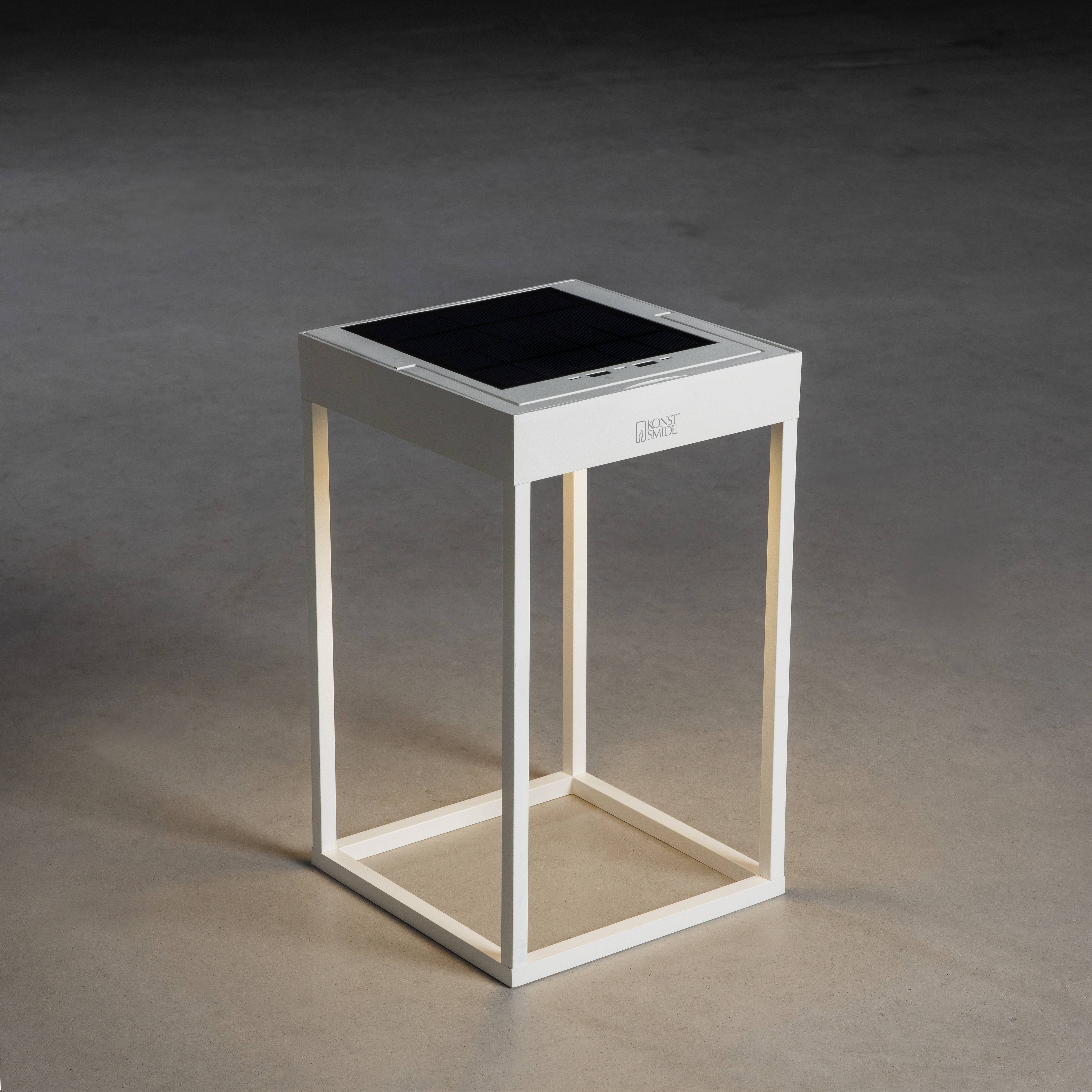 Une table blanche, carrée, avec un panneau solaire sur le dessus, est posée sur un sol gris. Éclairage sur la face intérieure.