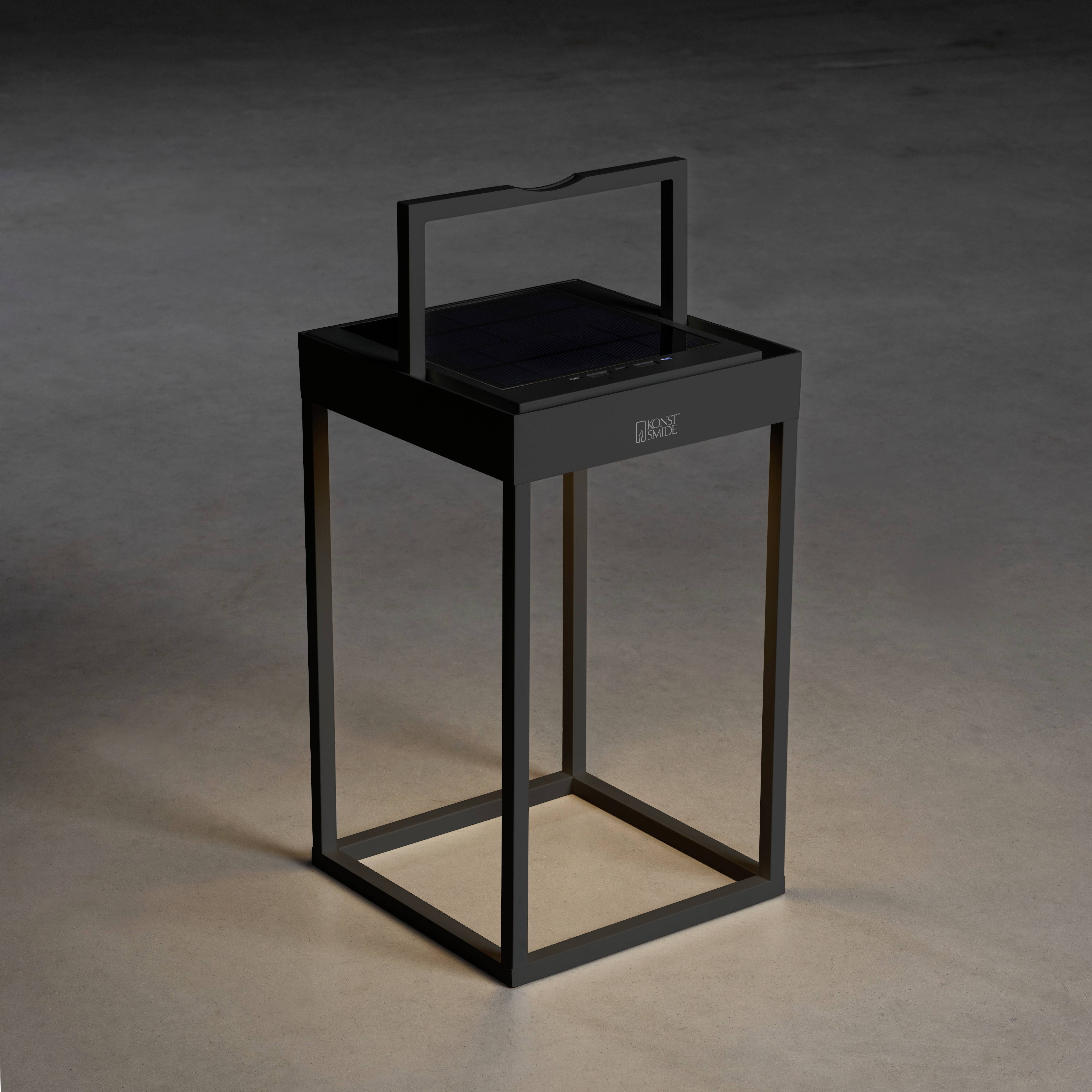 Une lanterne moderne, carrée, diffusant une lumière discrète sur le sol. Elle se trouve dans une pièce sombre.
