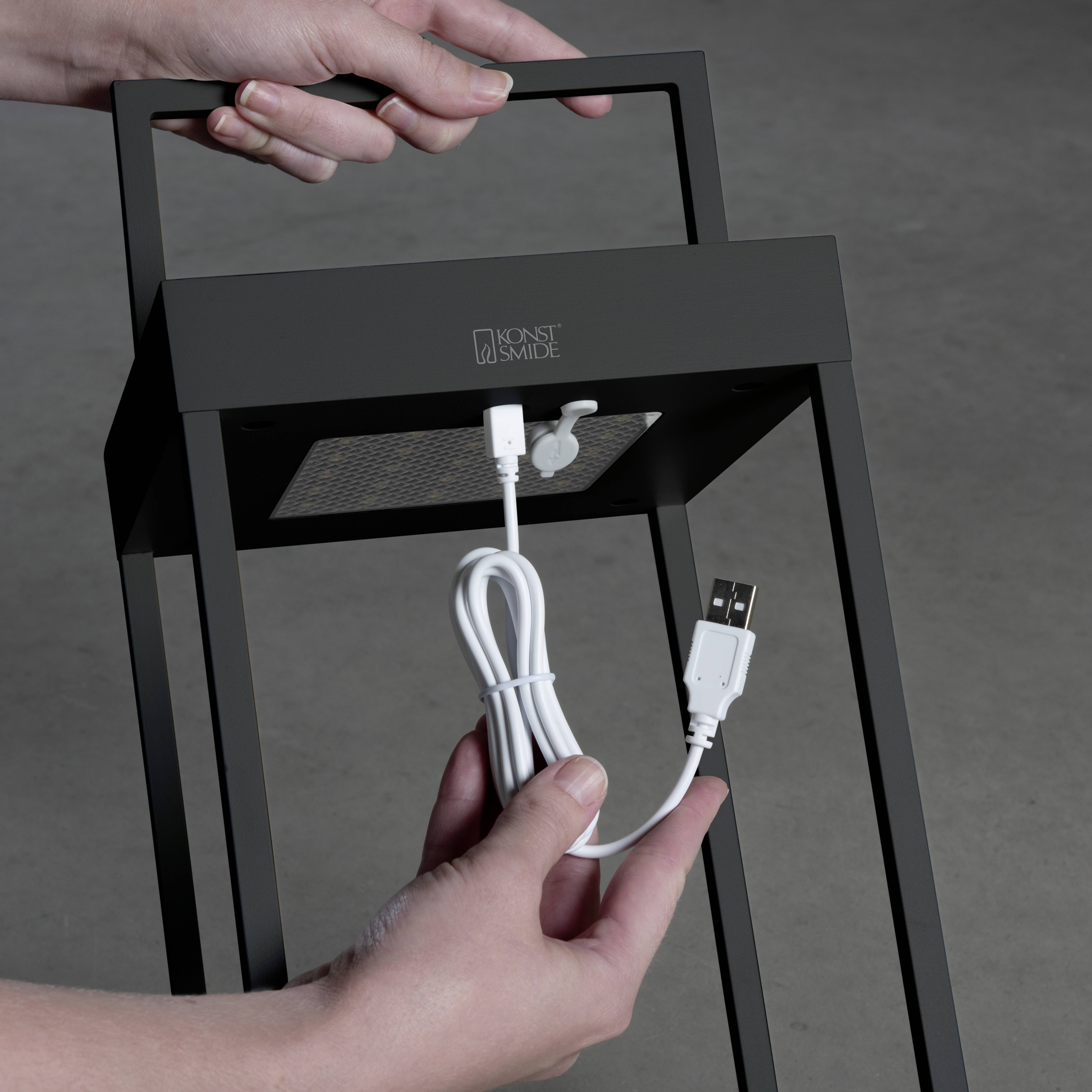 Une personne tient un support métallique noir rectangulaire avec un câble USB branché à une ouverture supérieure dans un luminaire.