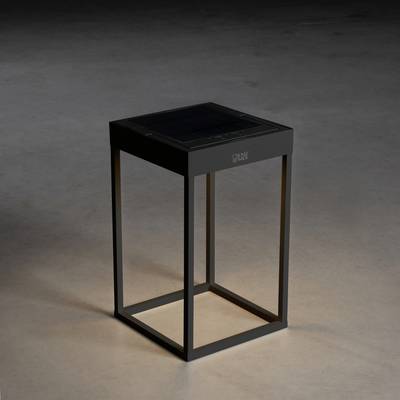 Une table élégante, carrée, avec un châssis sombre est posée sur un sol gris. La table a une surface lisse et noire.