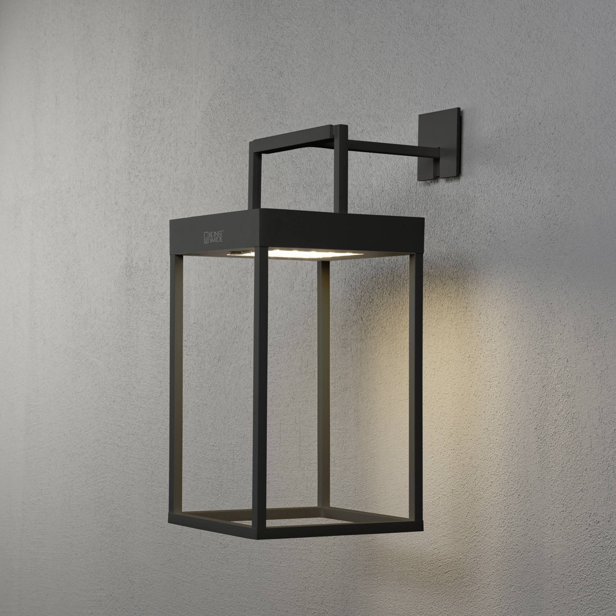 Un luminaire extérieur moderne rectangulaire avec un cadre noir, installé sur un mur gris, éclaire la zone située en dessous.